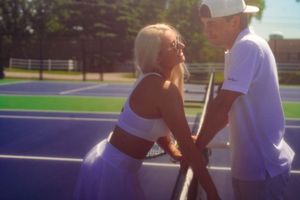 Tennis players share a romantic moment by the net on an outdoor court during a bright summer day.