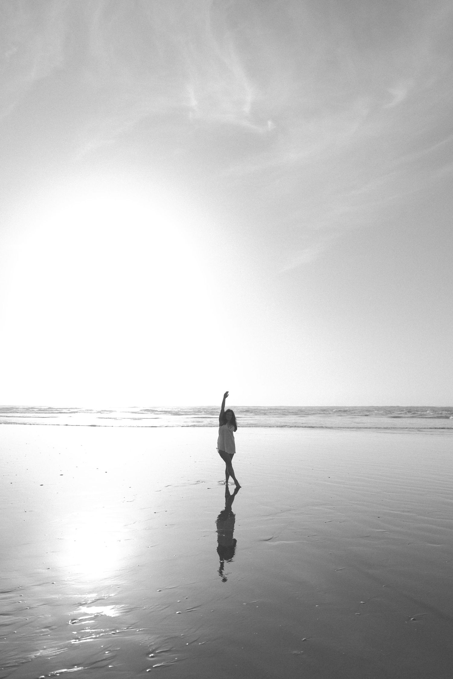 Black and white silhouette of a woman with arm raised reflected on a wet beach at sunset in New Zealand.