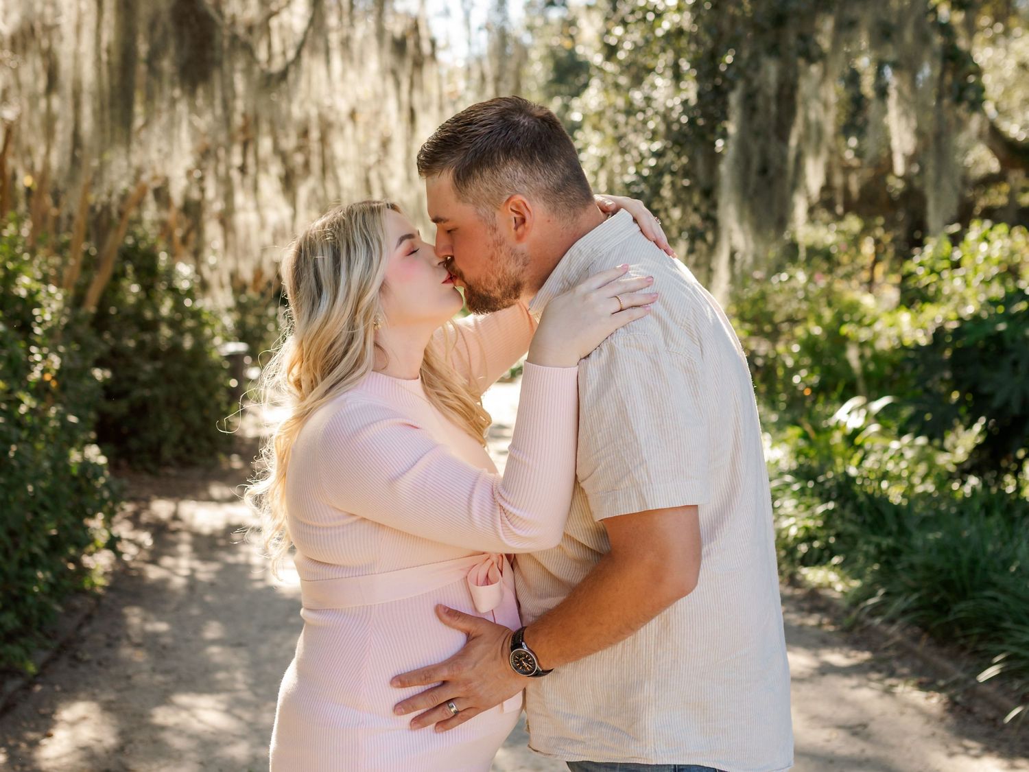 Romantic couple embracing in a sunlit wooded area with Spanish moss.