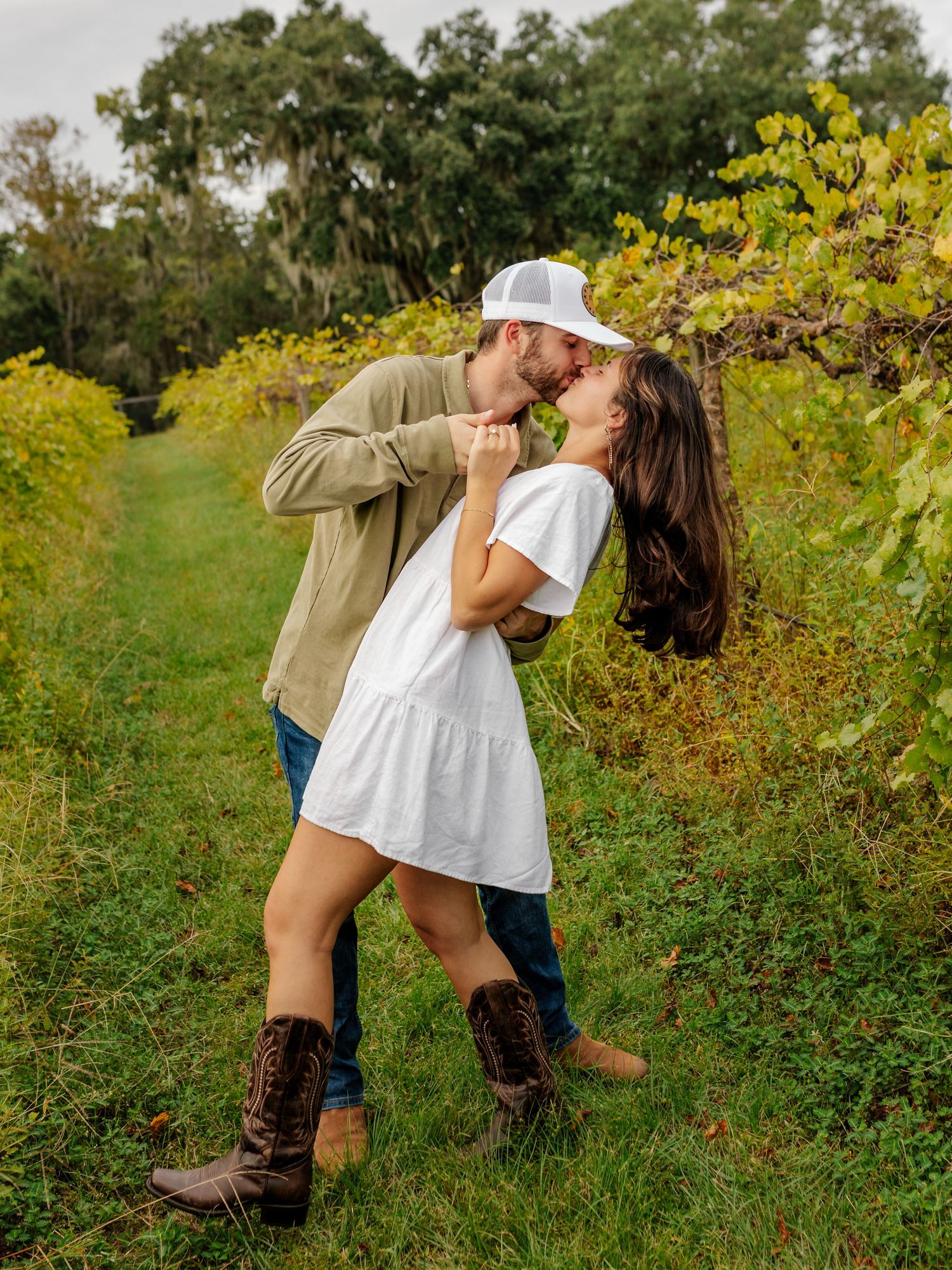 Couple in casual attire sharing romantic moments in a lush green field during golden hour.