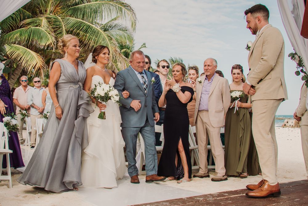 Wedding party gathers on a tropical beach with palm trees, wearing elegant gray and beige attire. El Dorado Royale Wedding Photographer