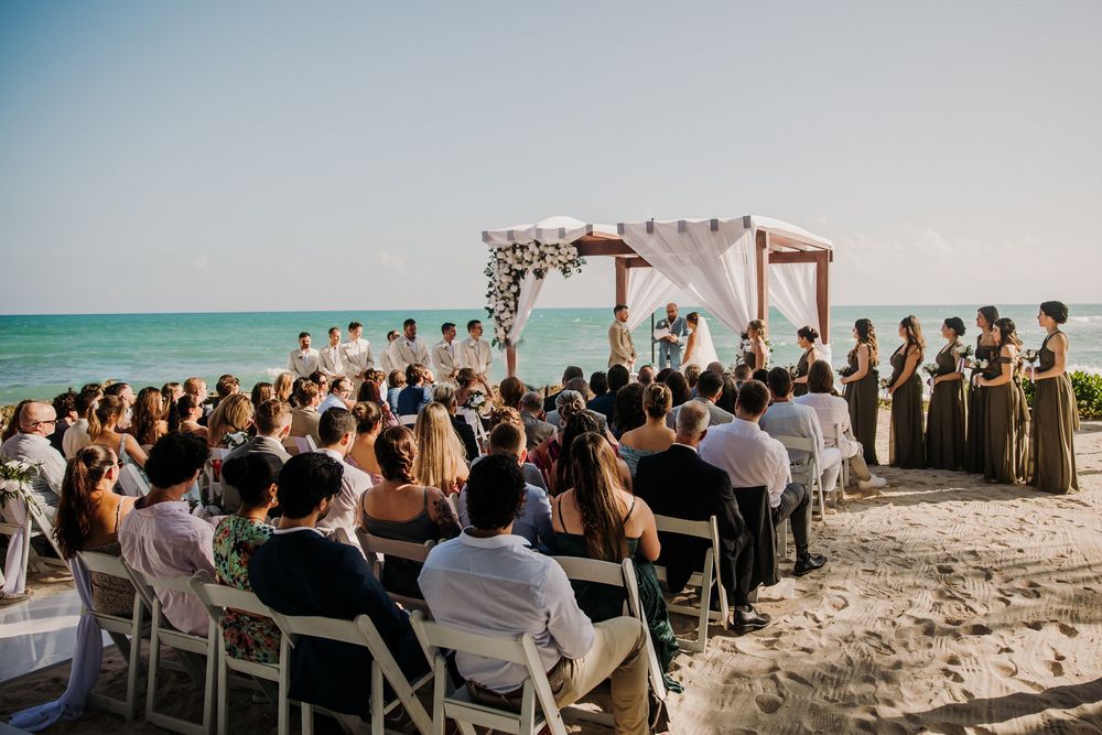 Beach wedding ceremony setup with wooden arch and white fabric overlooking turquoise ocean waters. El Dorado Royale Wedding Photographer