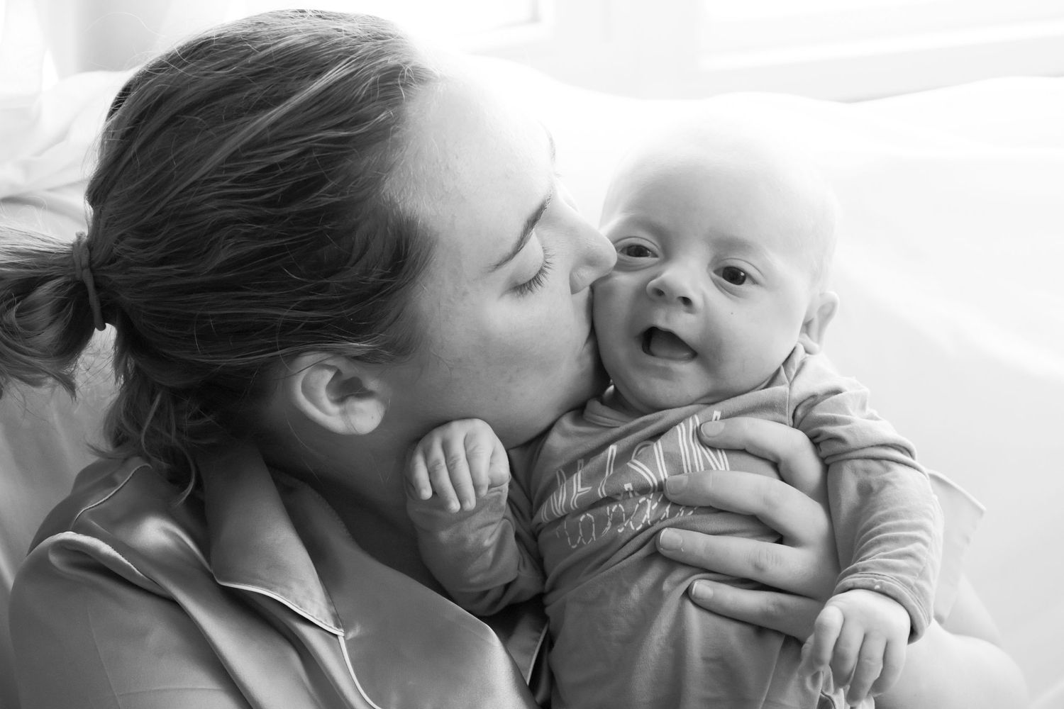 A tender black and white collage of intimate parent and baby moments showing gentle kisses and cuddles.