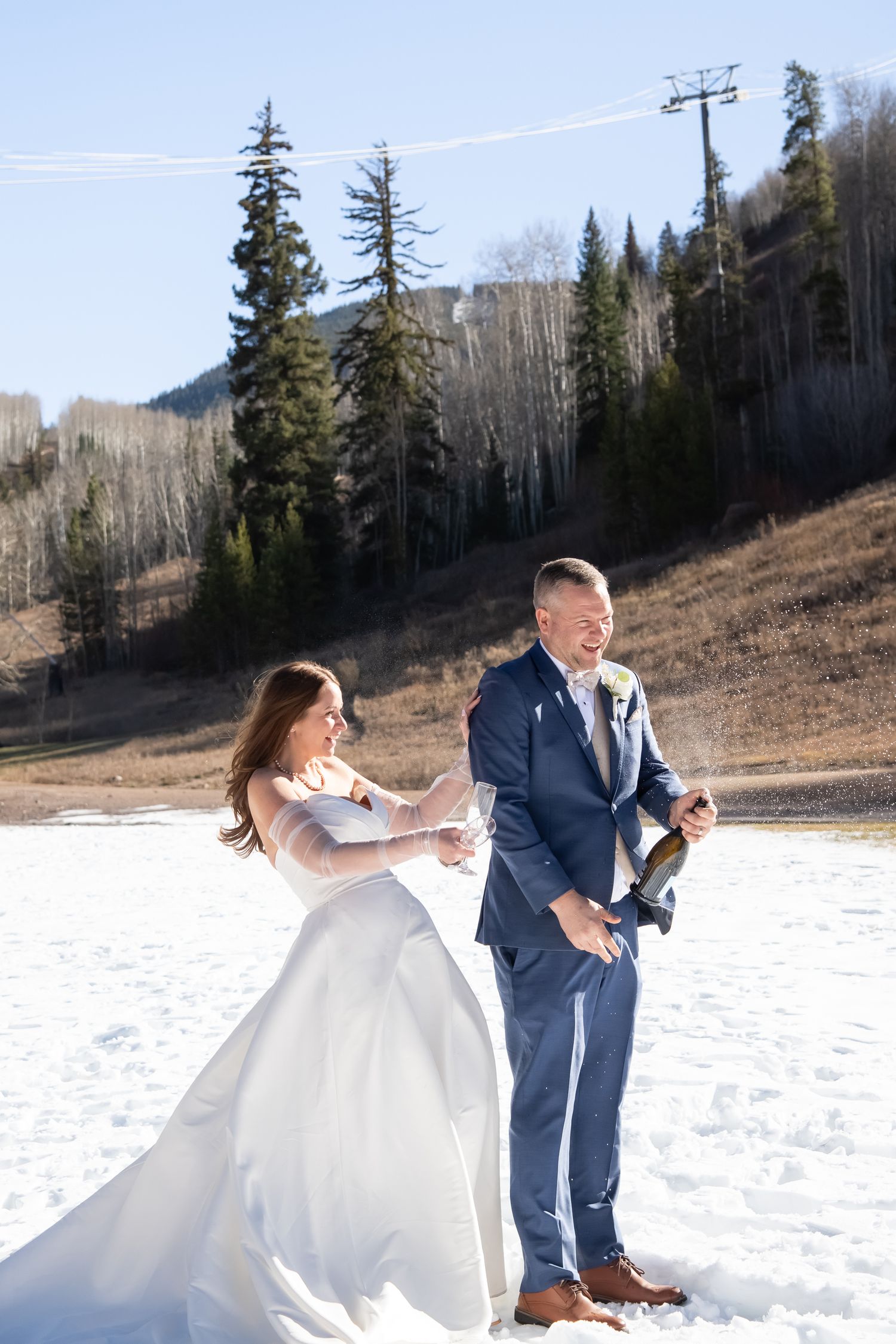 Bride and groom pop a bottle of champagne on snow after at wedding in Vail Colorado