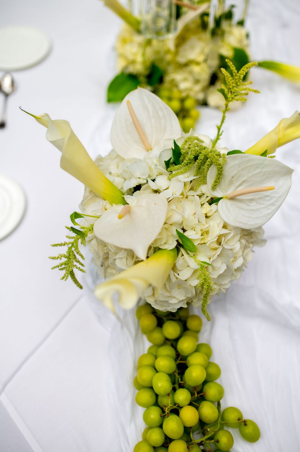 White floral arrangements with green grapes create an elegant table setting against a light background.