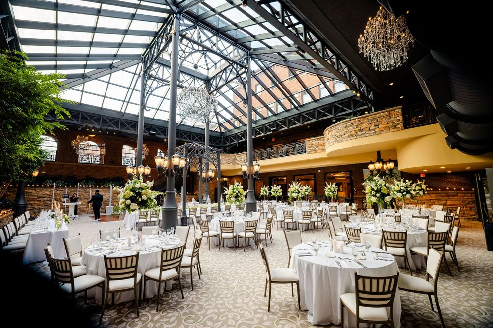 Elegant wedding reception venue with glass ceiling, crystal chandeliers, and white table settings in a garden atmosphere.