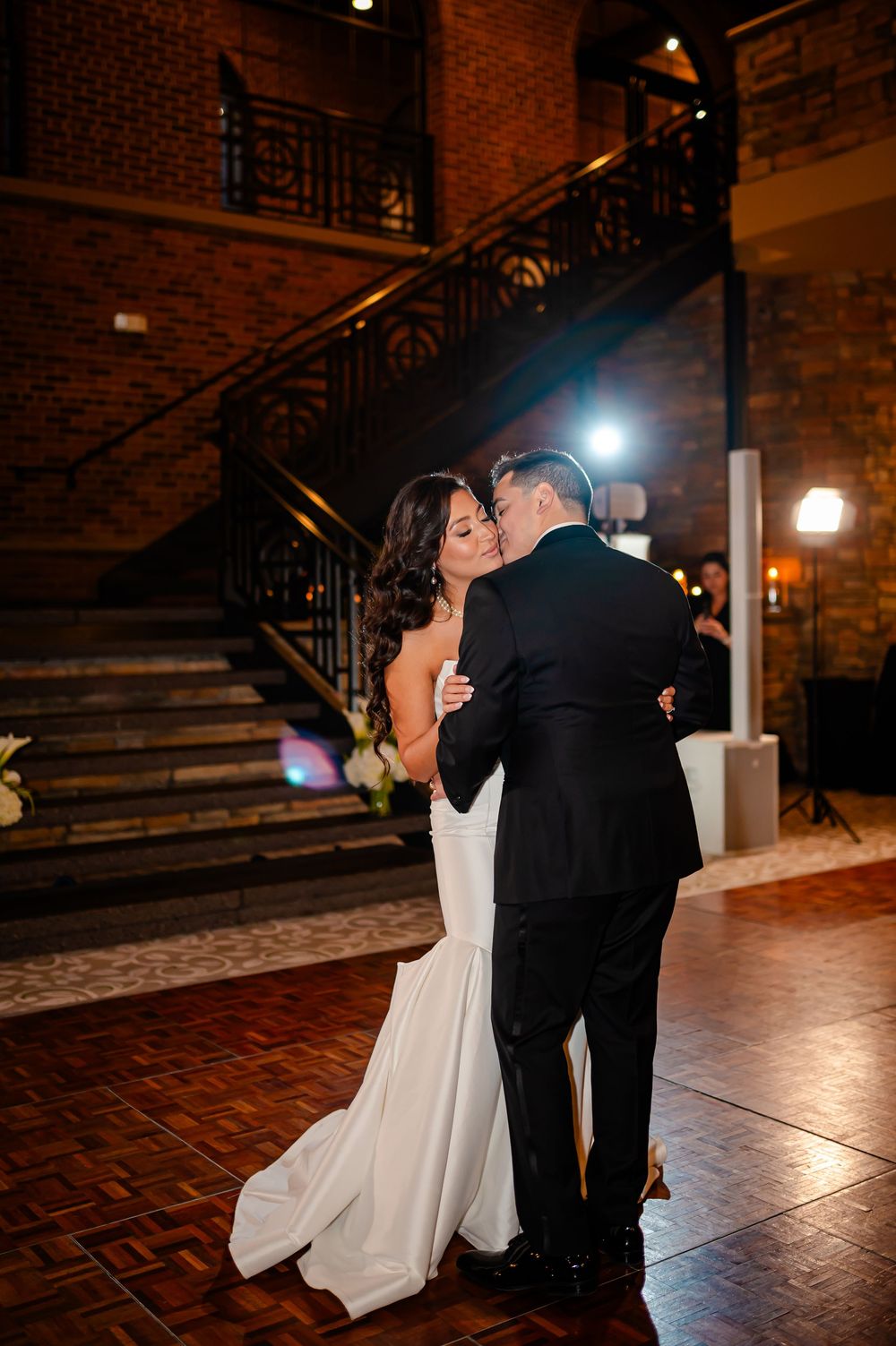 A couple shares their first dance at a wedding reception in a rustic brick venue with romantic lighting.
