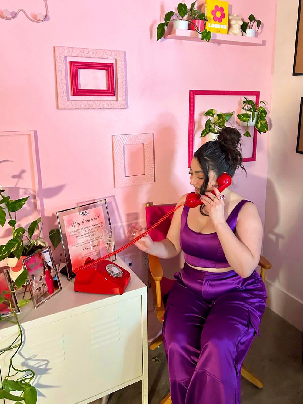 a young woman dressed in purple, answering a red rotary phone