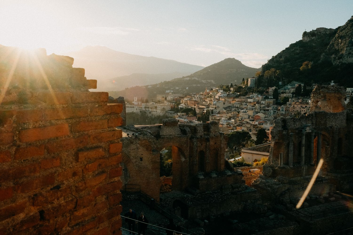 Ancient stone buildings and architecture silhouetted against a warm sunset in a mountainous landscape.
