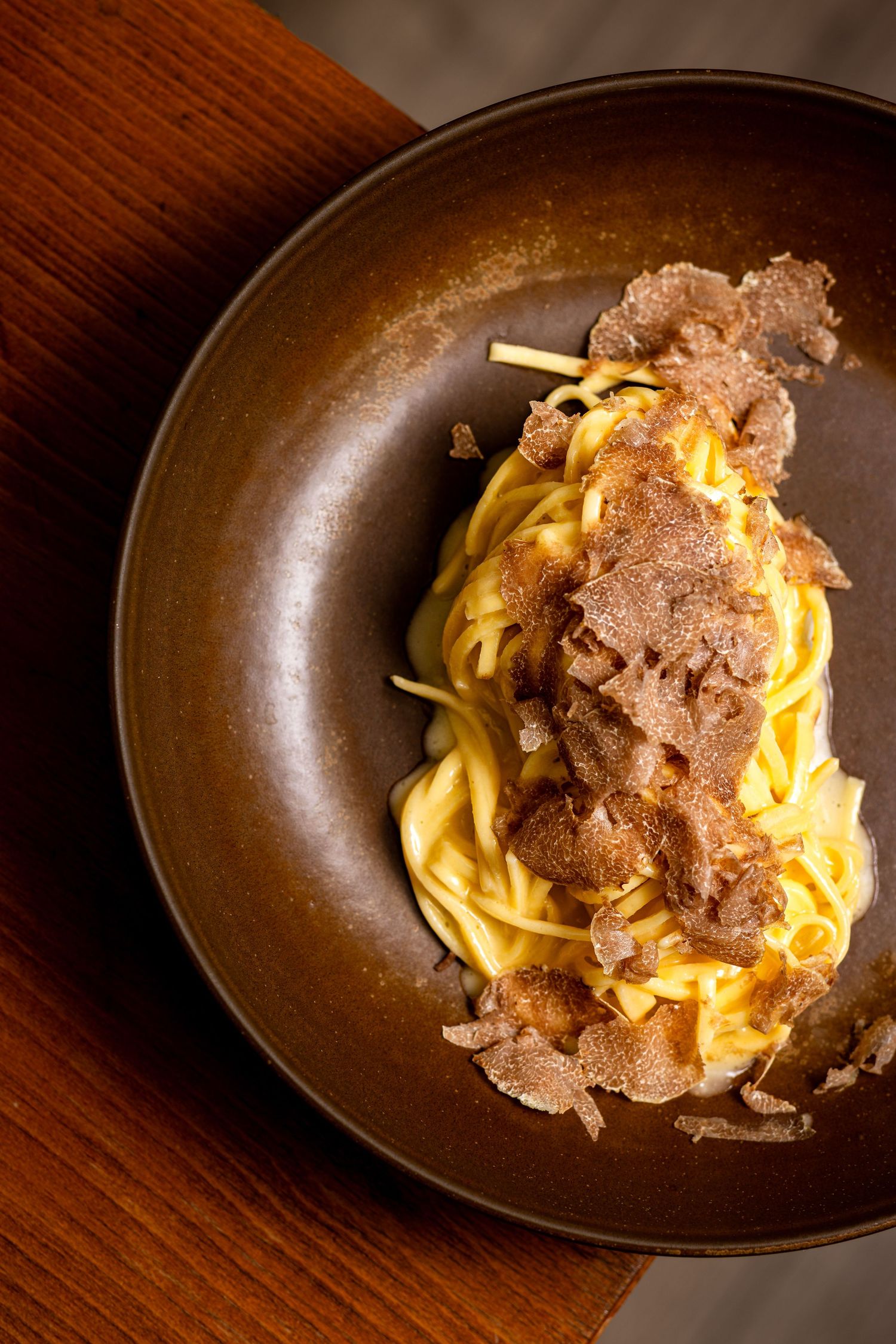 Fresh pasta dish topped with shaved black truffles served on a dark brown ceramic plate. Vidéo culinaire et storytelling visuel pour marques