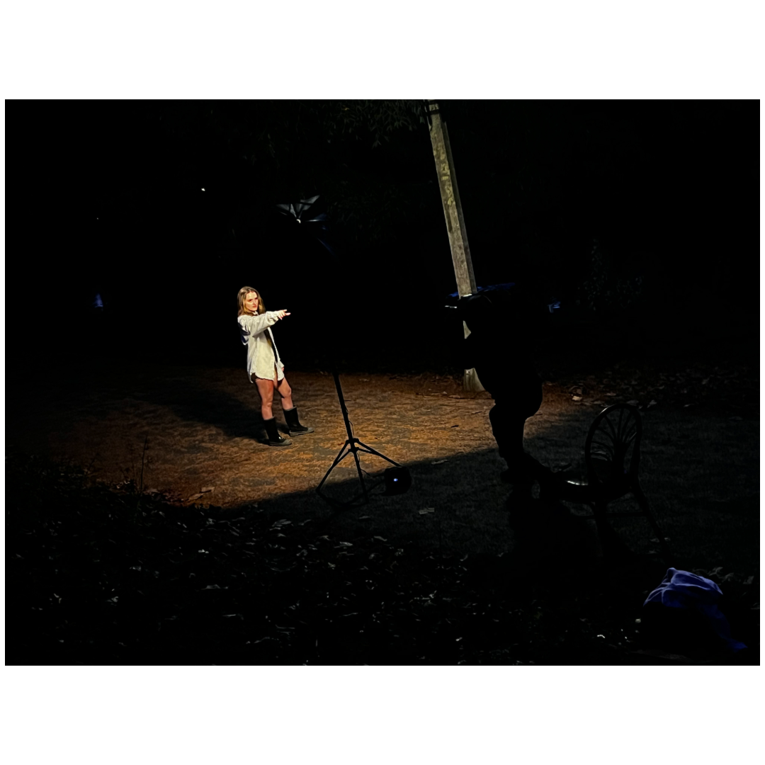 A person stands illuminated on a dark stage with dramatic spotlight creating a theatrical performance atmosphere.