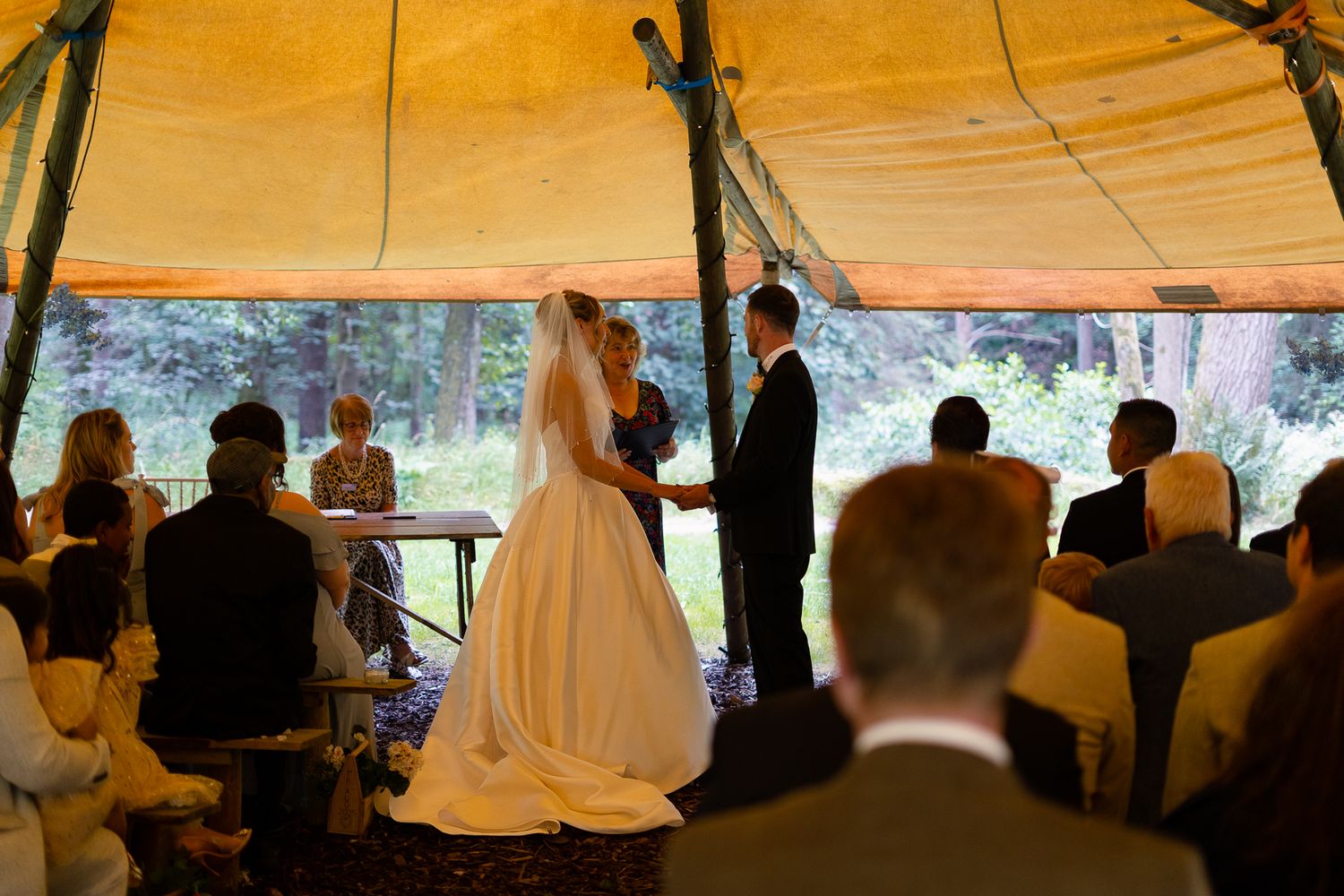 Wedding guests gather under a yellow tent canopy during an outdoor celebration at dusk.