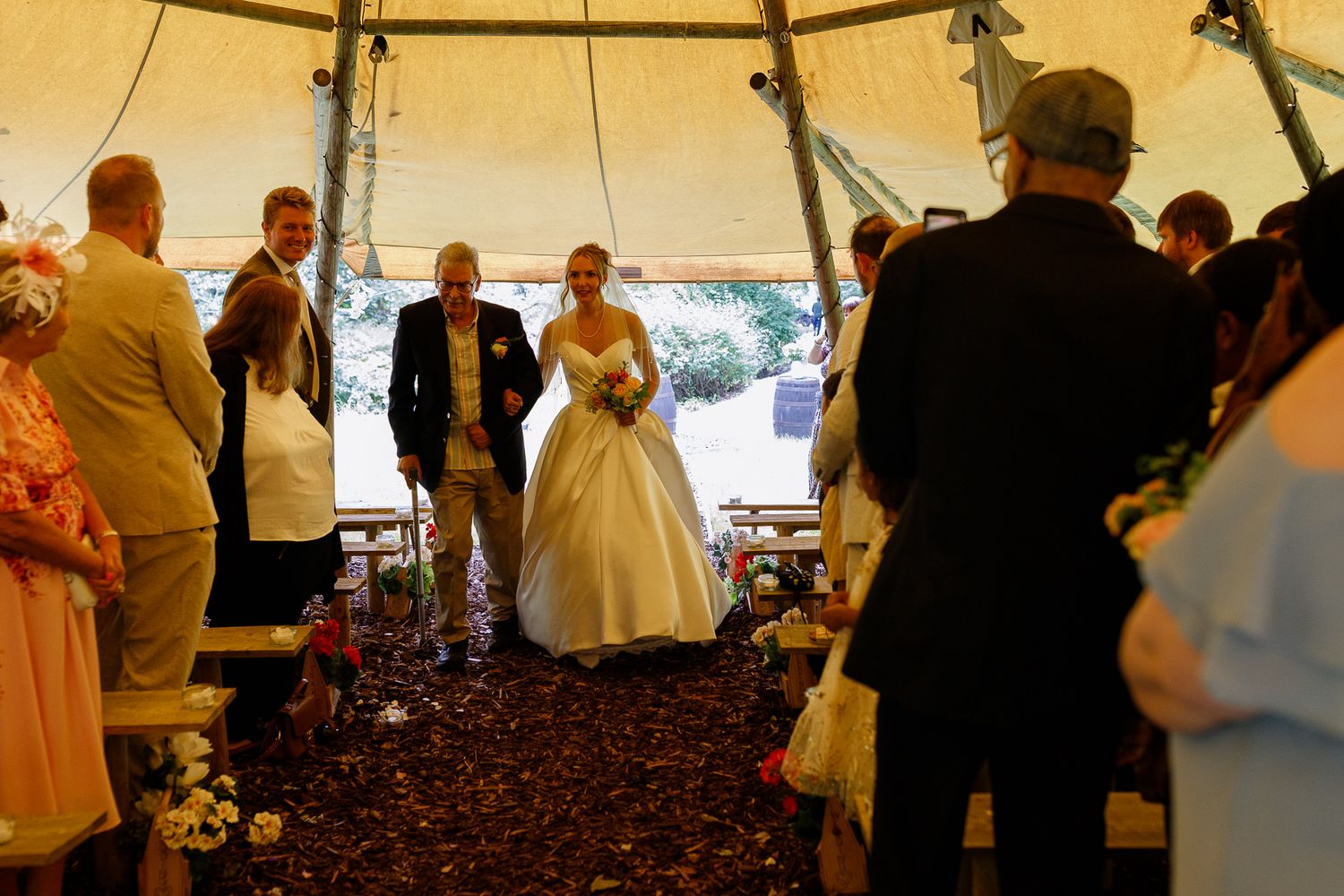 People gather under a large white tent for a social event with tables and chairs visible in the background.