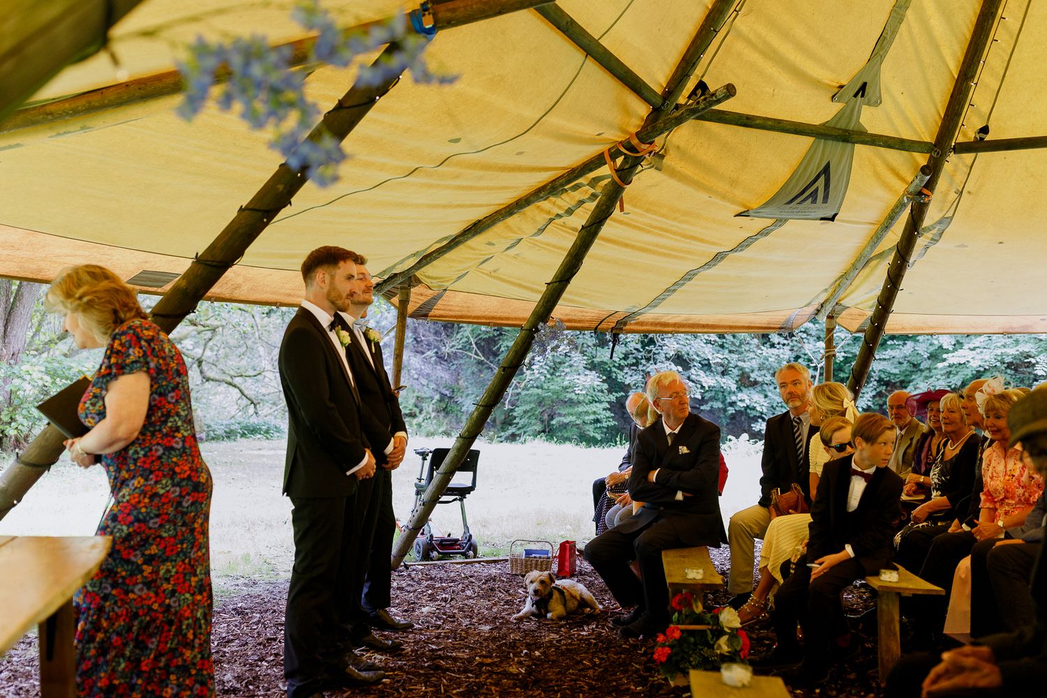 Wedding guests dance and celebrate under a large white outdoor tent during an evening reception.