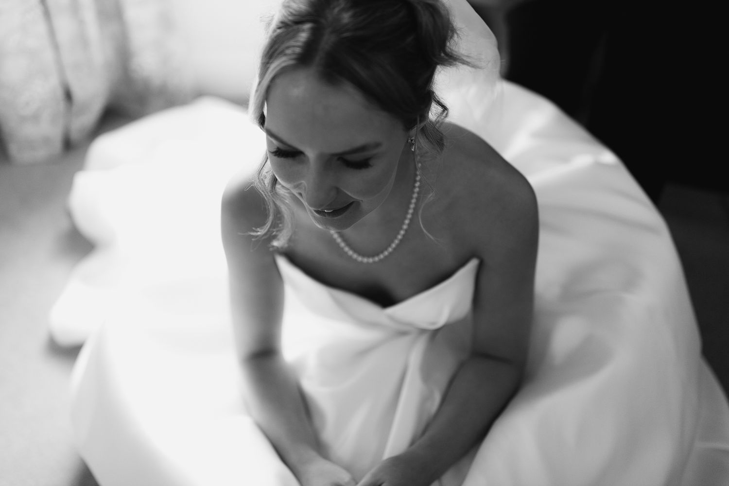 Black and white photograph of a bride in a white wedding dress looking down with a gentle smile.
