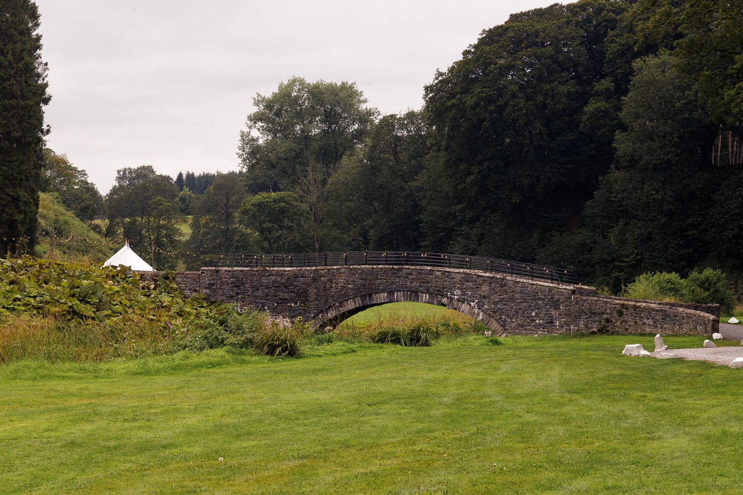 Rolling green hills and trees create a scenic landscape view with a stone bridge in the distance.