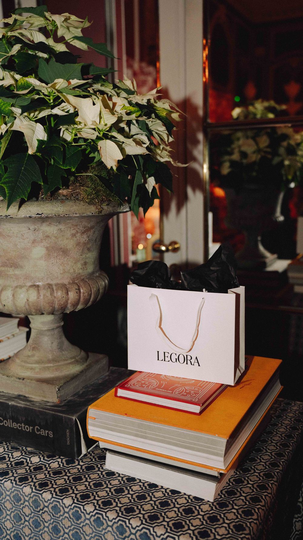 Detalle de mesa decorada con libros apilados, planta y bolsa de marca durante evento