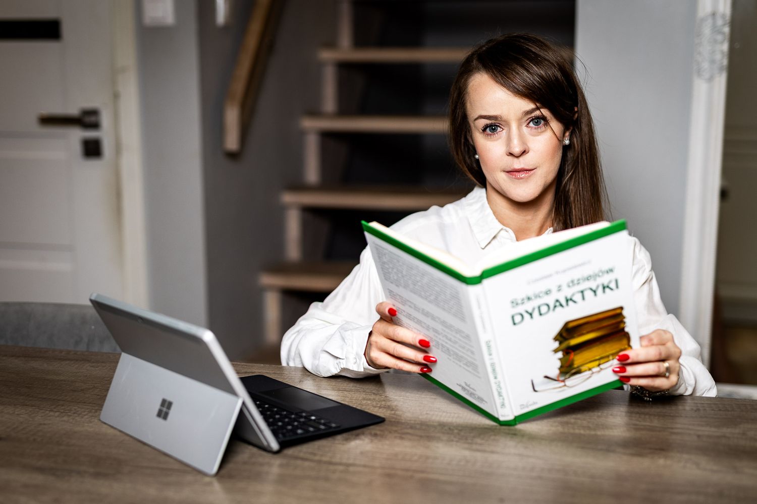 Person reading a white book while sitting at a desk in a well-lit room.