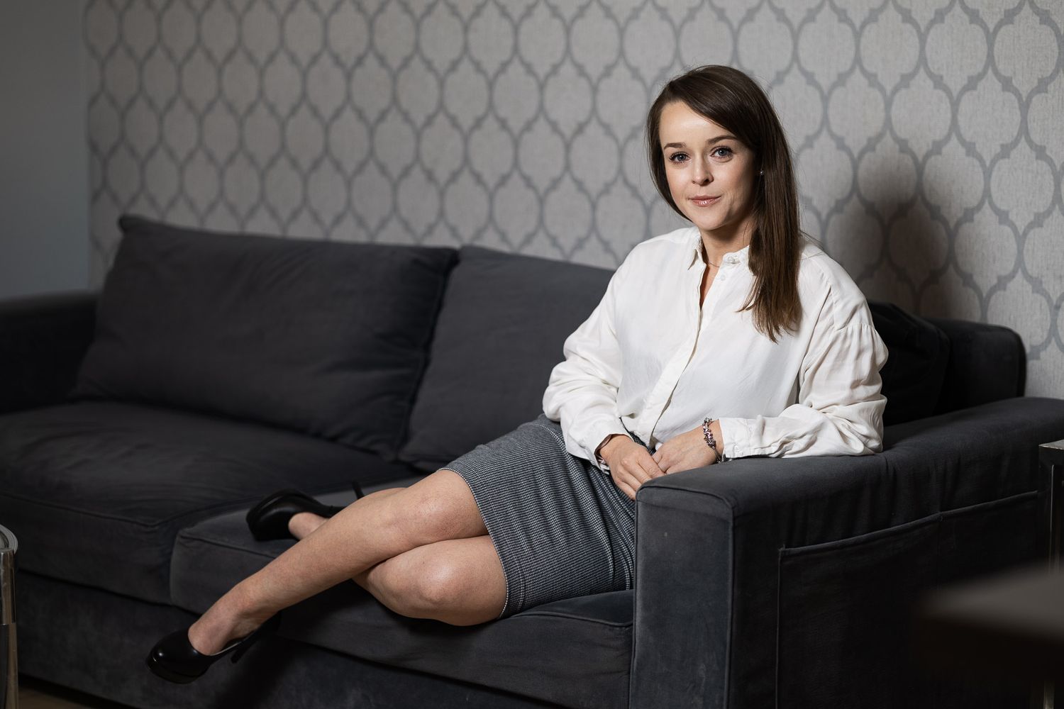 Person in business attire relaxes on dark couch during professional photoshoot.