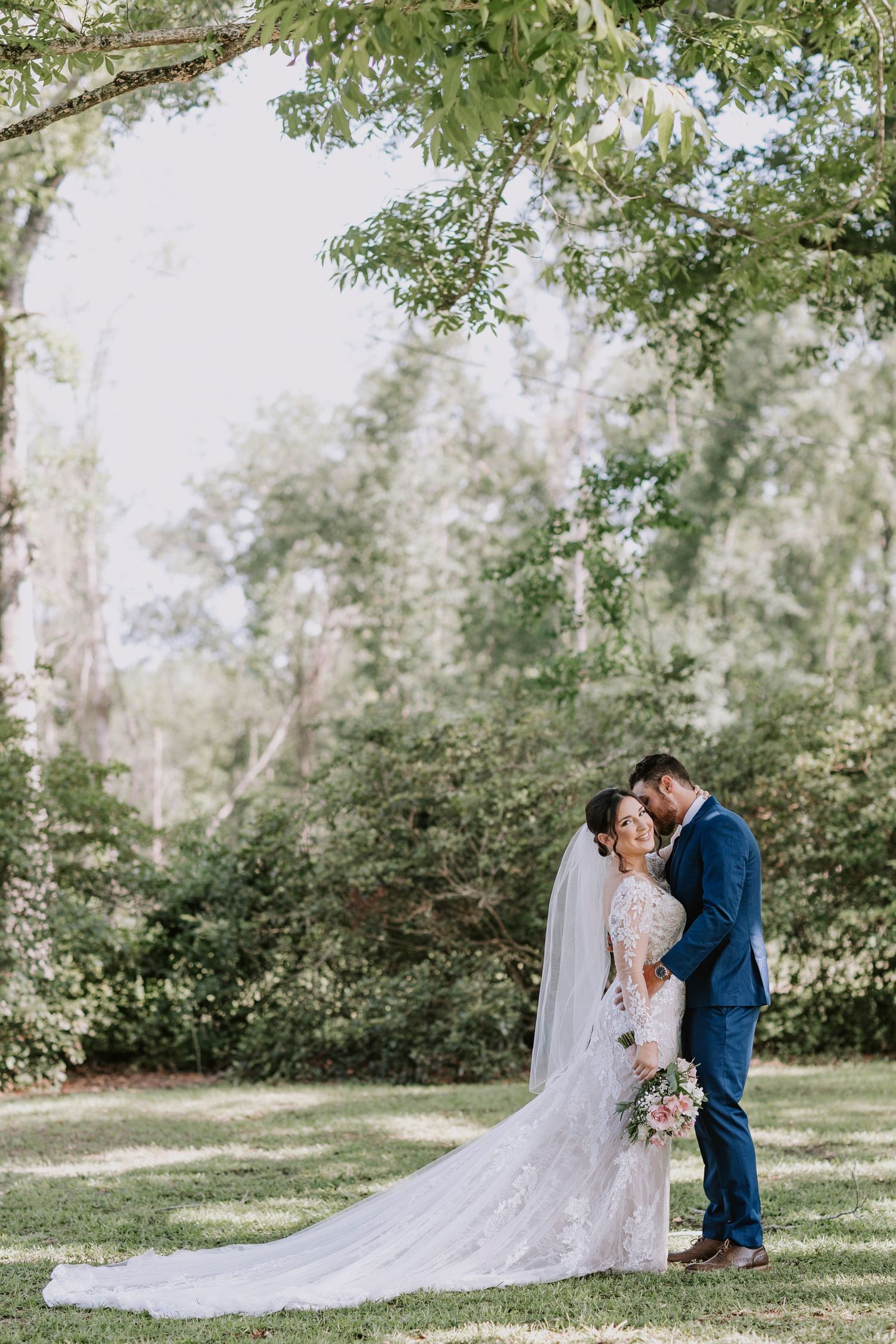 Newlywed couple share intimate moment in garden setting with flowing lace wedding dress.