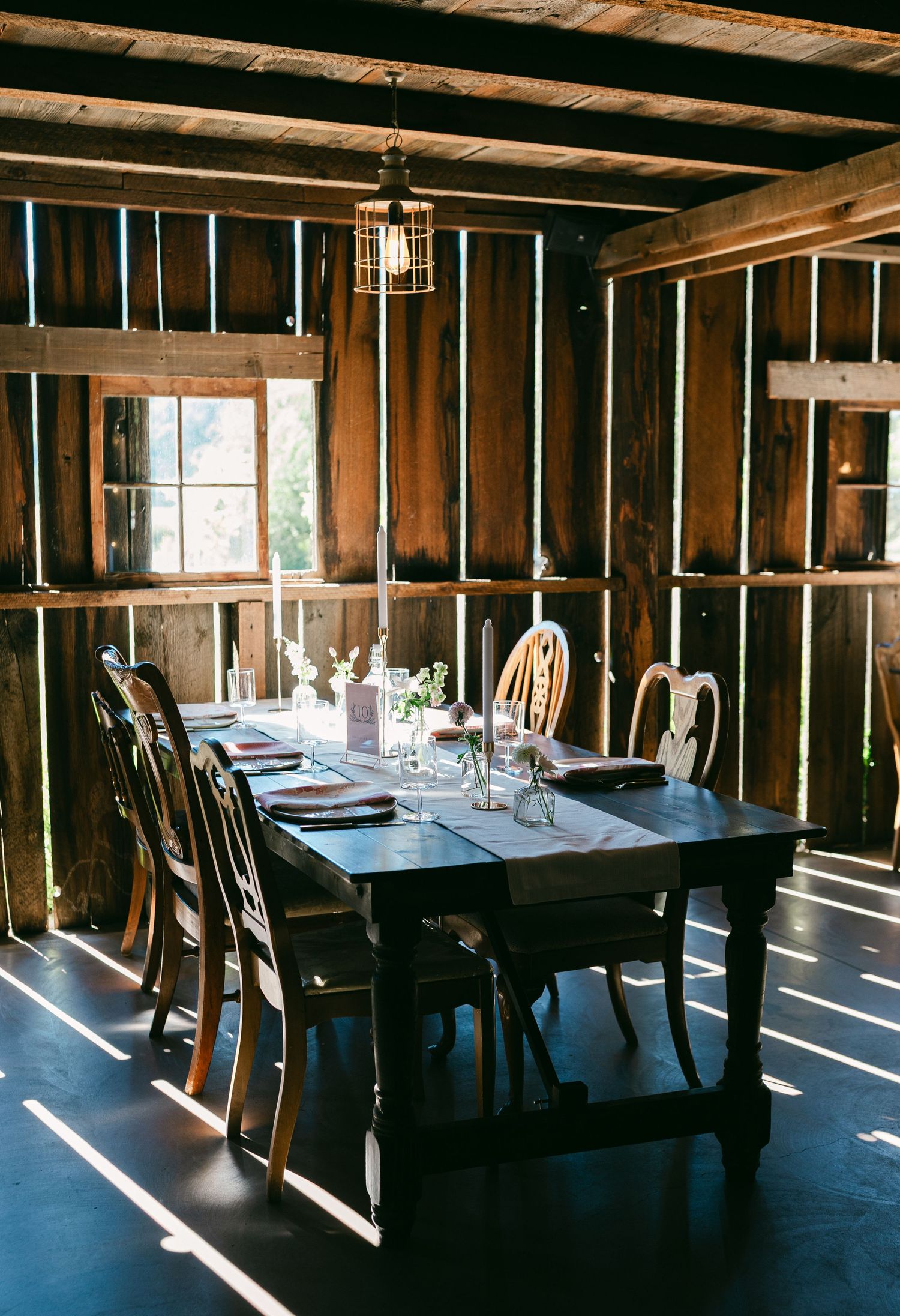 Rustic dining room interior with wooden walls and tables set for service as sunlight streams through windows.