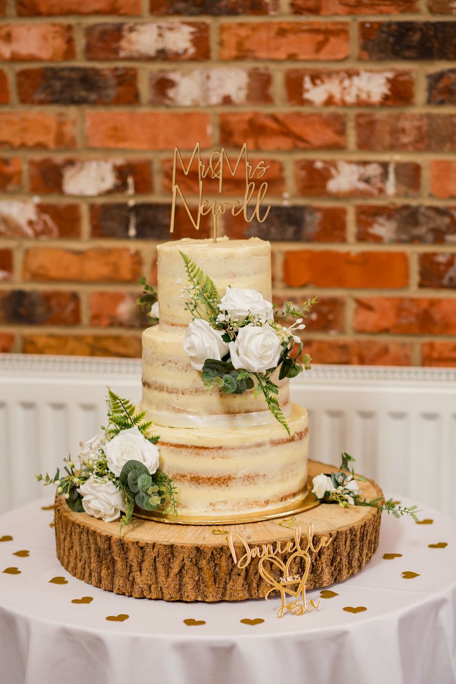 Rustic naked wedding cake decorated with white roses on wooden slice stand.