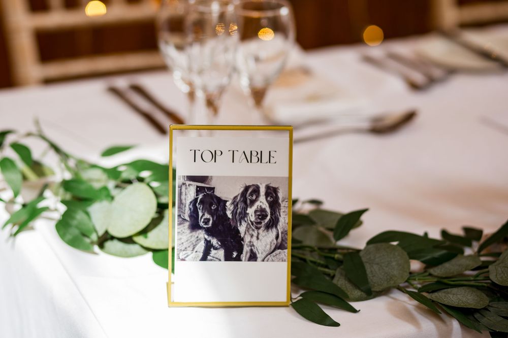Elegant wedding reception table setting with greenery and framed photos.