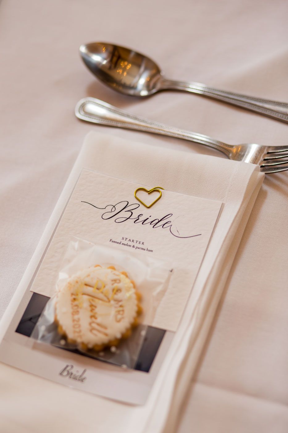 Place setting with bride name card and heart detail on white tablecloth.