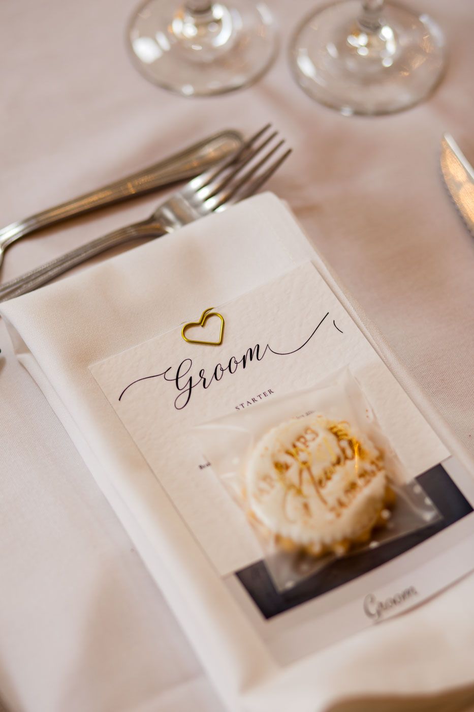 Wedding place setting featuring groom name card and decorative cookie.