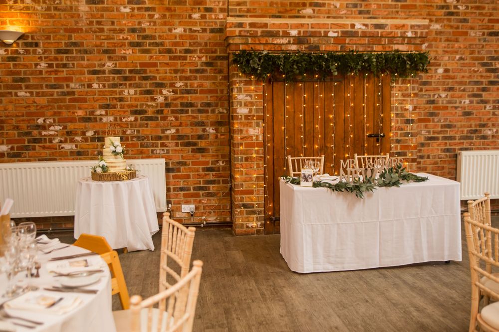 Rustic brick wall wedding venue with white draping and wooden chairs.