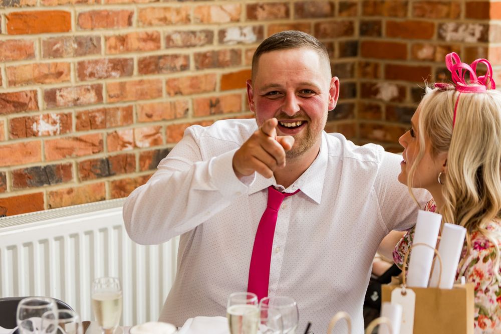 Wedding reception guests seated at tables with pink accent decor.