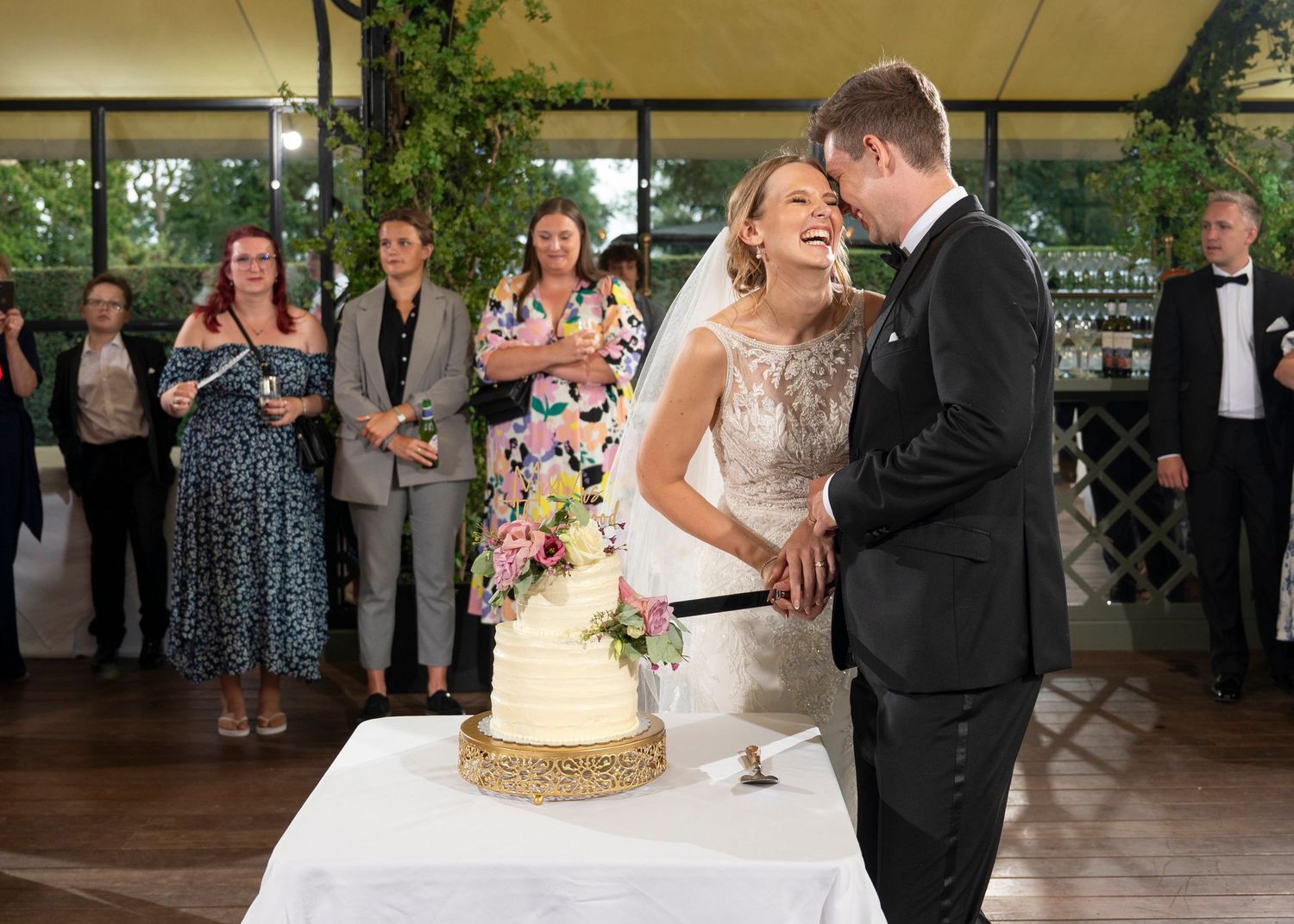 Wedding couple and guests dance together under a covered outdoor pavilion during an evening reception celebration.