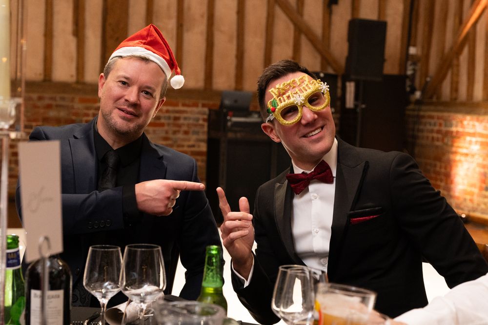 Two party guests at a holiday dinner wearing festive accessories and formal attire share a lighthearted moment.
