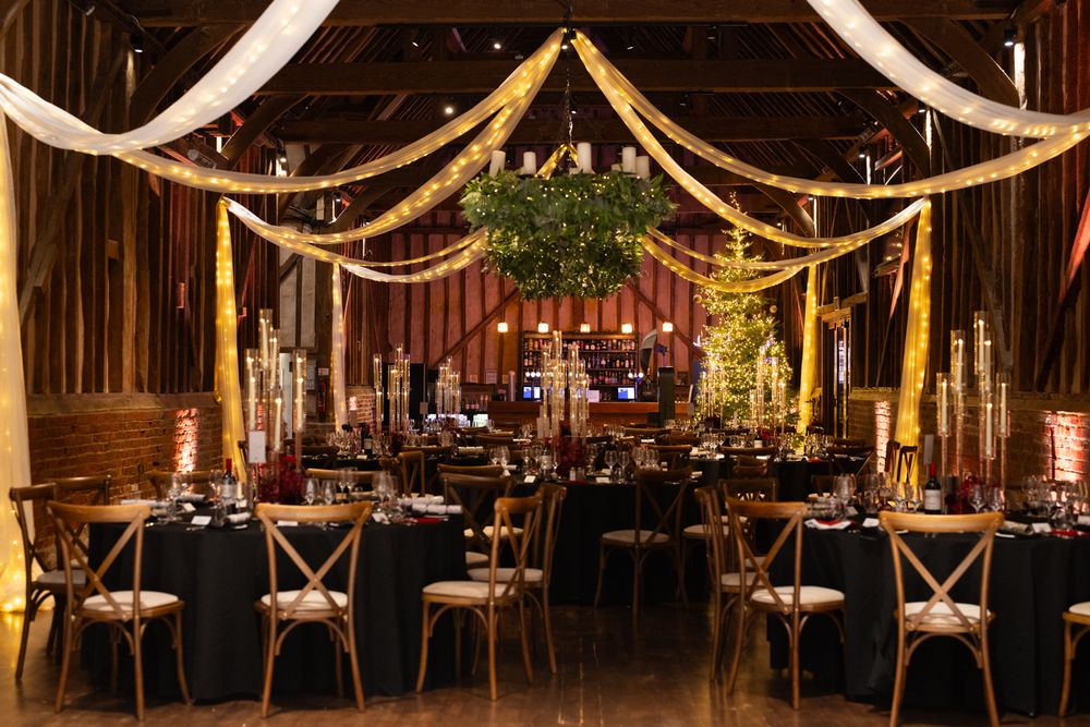 Elegant rustic wedding reception venue with wooden beams, string lights, and cross-back chairs creating a warm ambiance.