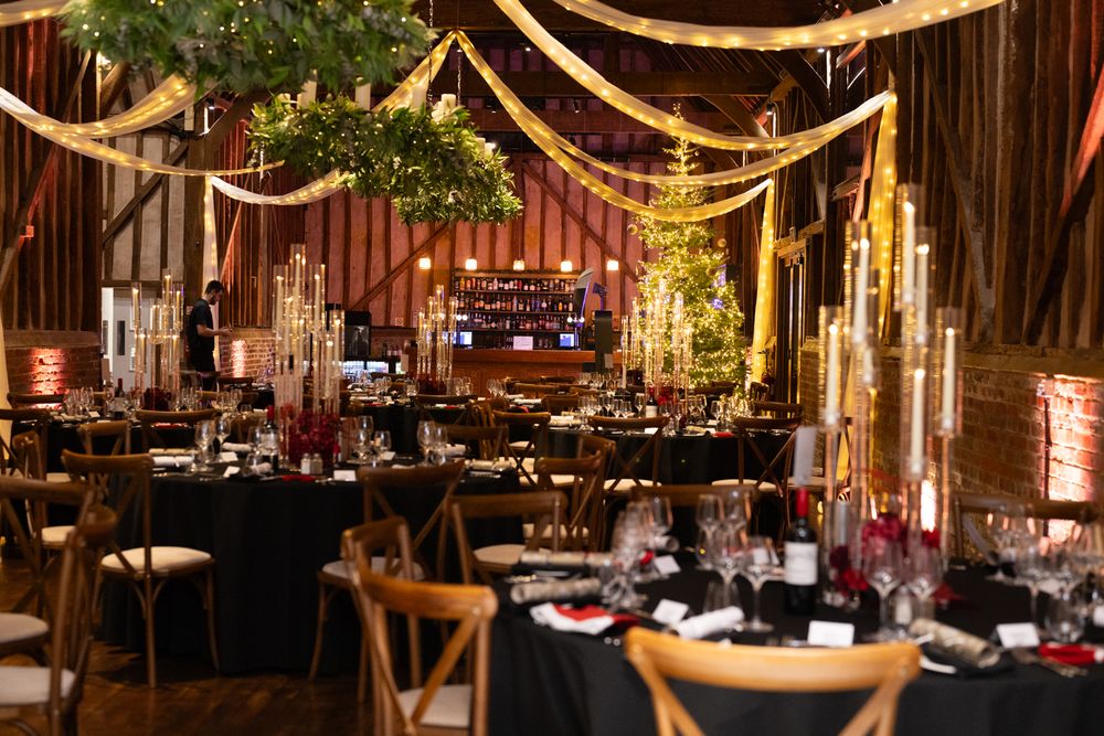String lights illuminate a rustic barn wedding reception with wooden tables and elegant table settings.