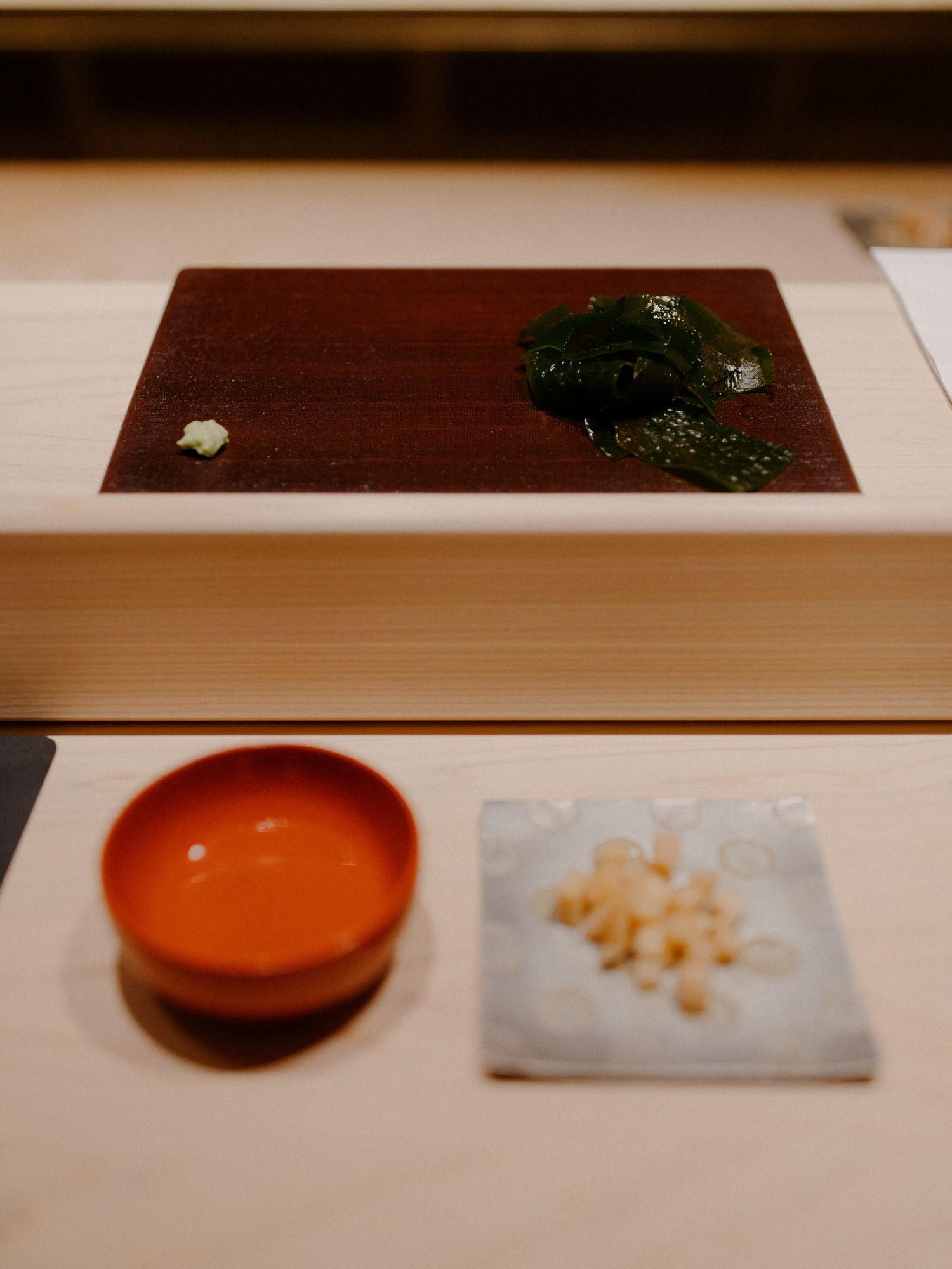 Minimalist dining presentation with orange bowl and small cubed garnishes on wooden surface.