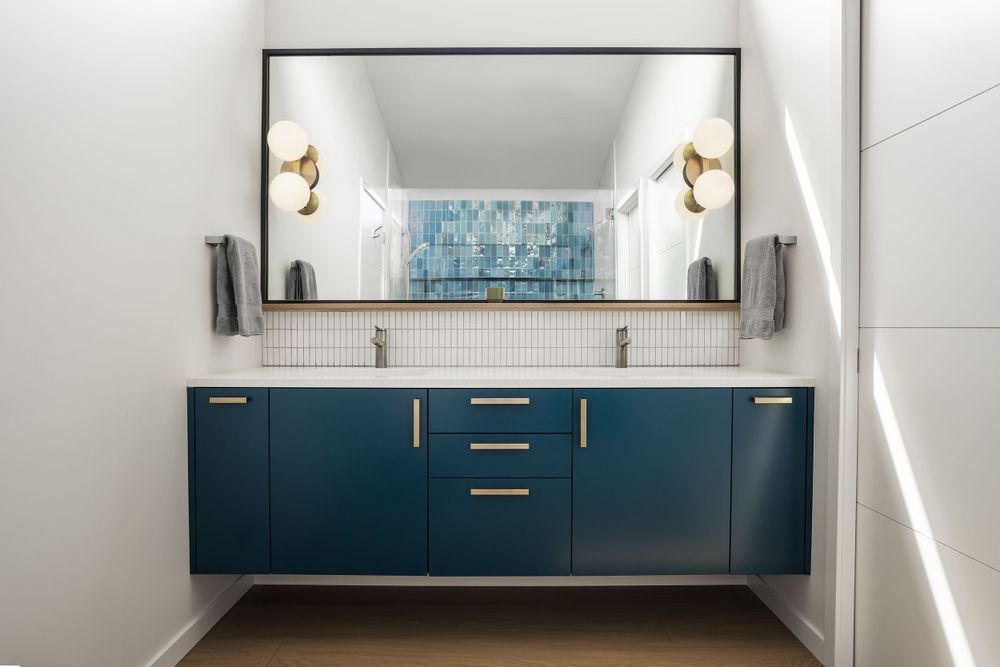 Modern bathroom with sleek blue cabinetry, double sinks, and a large mirror reflecting a shower with bold blue tilework.