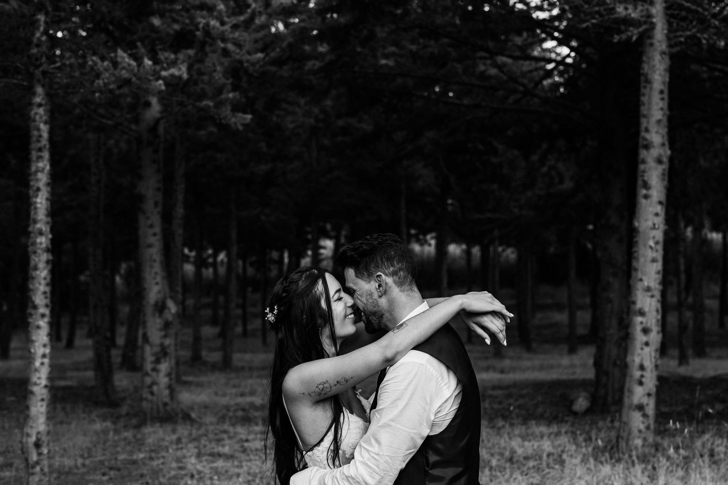 A romantic black and white photo of a couple embracing in a wooded forest setting.