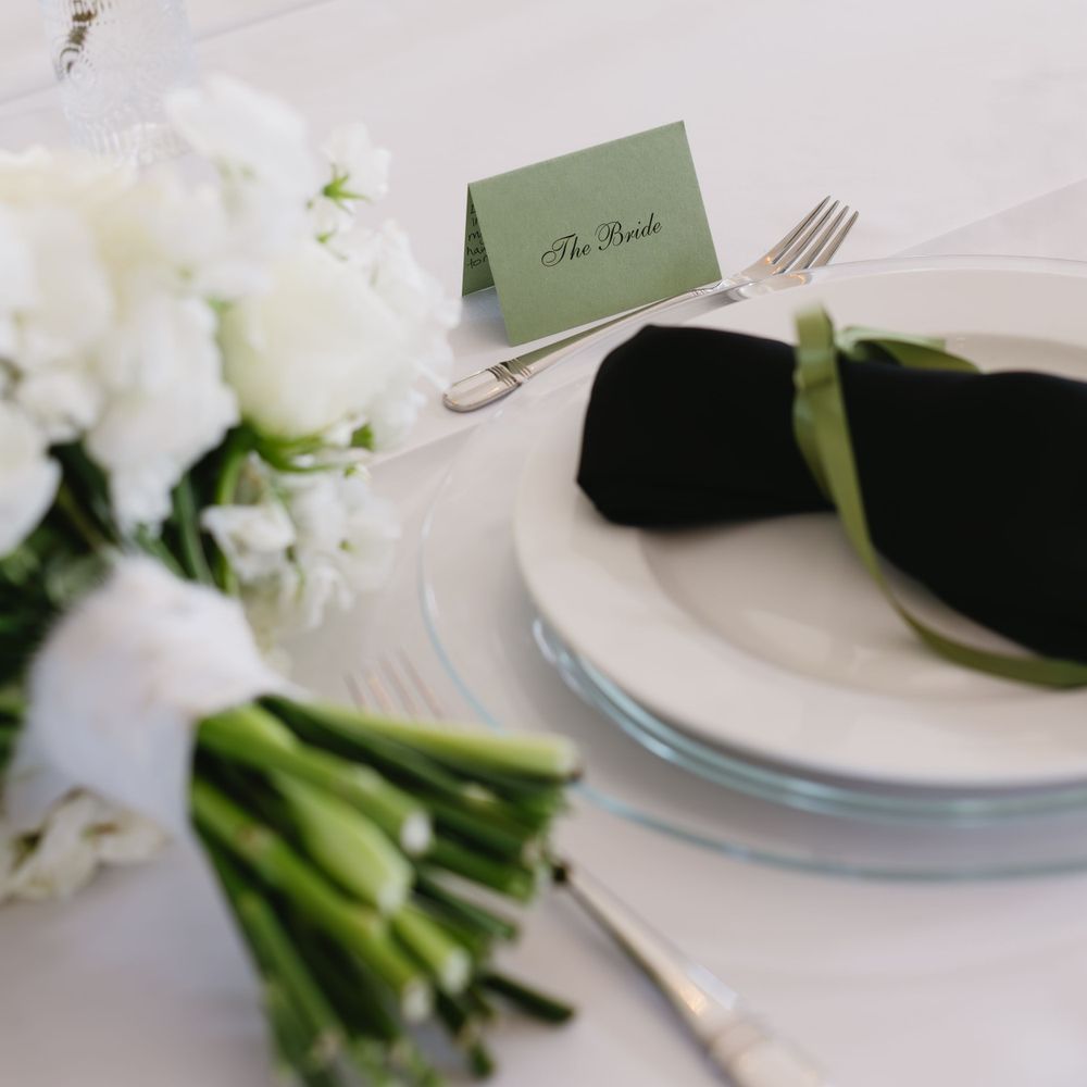 An elegant place setting with a green name card, black napkin, and white floral centerpiece at a formal event.