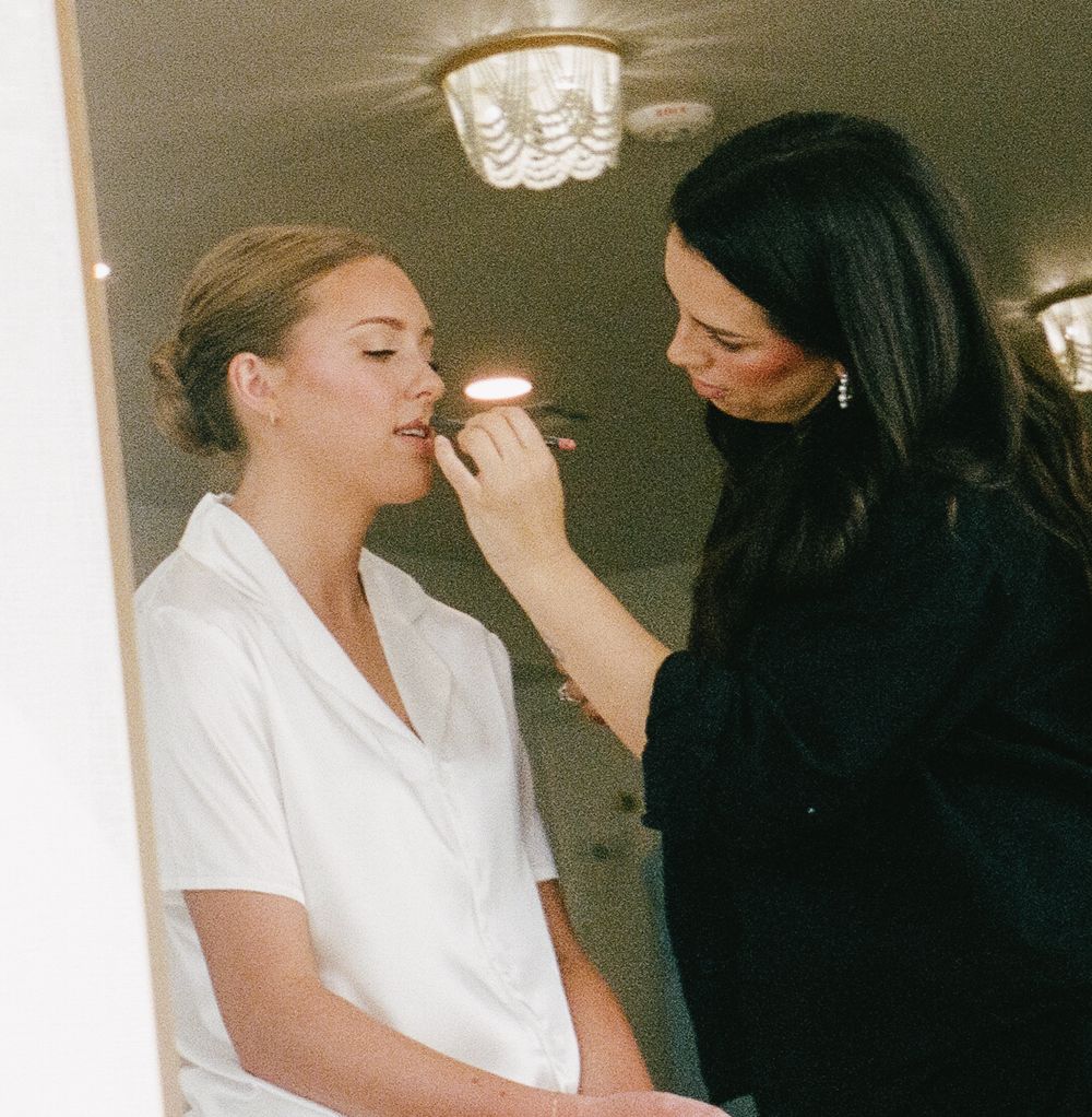 Makeup artist applying cosmetics to a woman in a white robe during a beauty preparation session.
