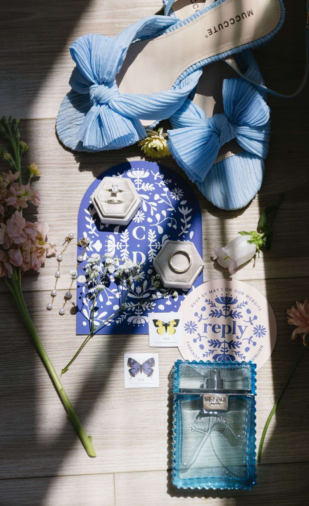 Elegant blue bow sandals with butterfly stationery and a perfume bottle arranged in natural lighting.