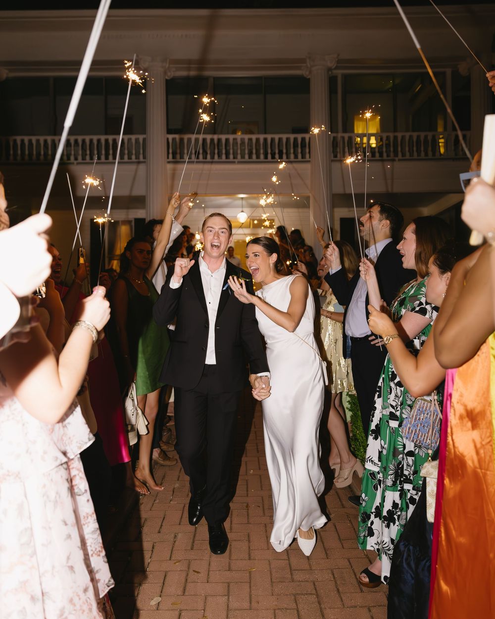 Wedding couple makes grand entrance under sparklers held by guests at evening reception.