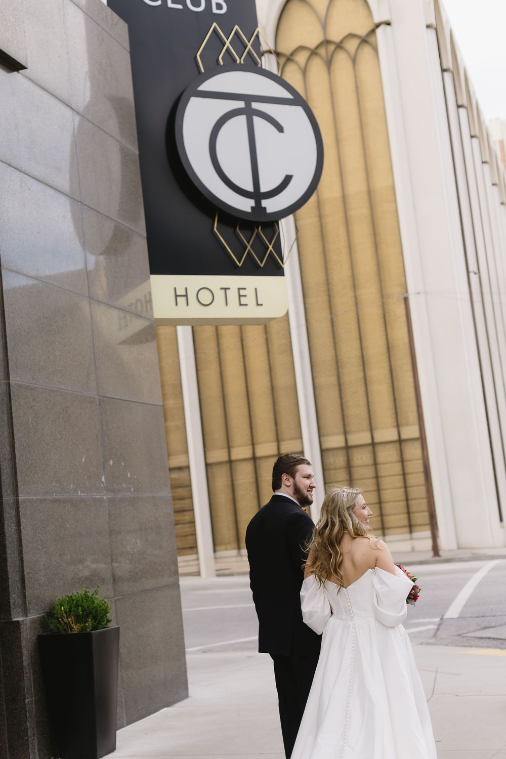 A couple in wedding attire stand together outside the TC Hotel with its distinctive art deco signage and architecture.