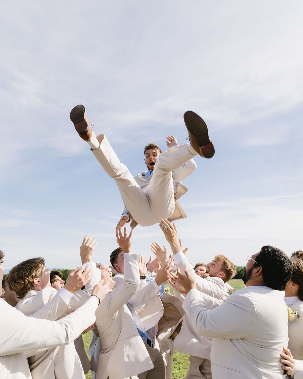 A group in white attire celebrates by tossing someone into the air during an outdoor celebration.