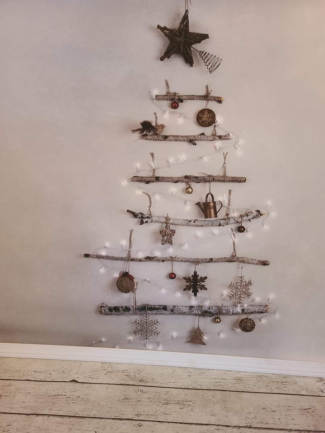 Minimalist wall-mounted Christmas tree made of wooden branches with rustic ornaments and star topper.