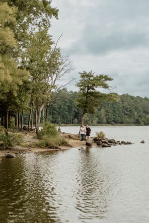 A distant view of people standing on a rocky shoreline surrounded by trees and water.