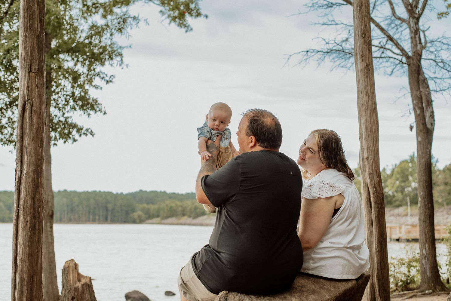 A group sits on a bench by a serene lake surrounded by trees during an outdoor photo session.