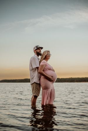 A romantic maternity photoshoot with the couple standing in lake water during sunset.
