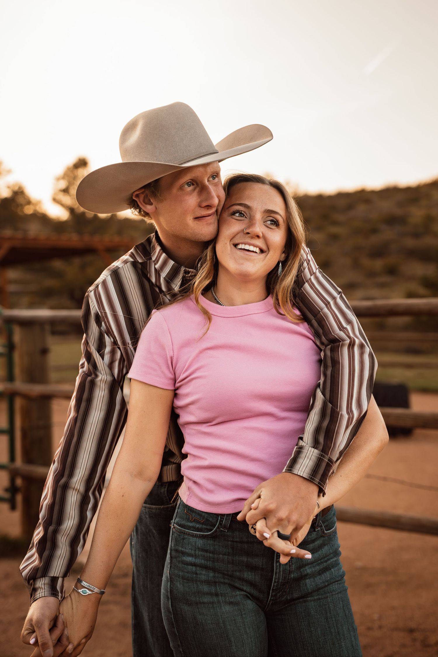 Figure in cowboy hat and vest poses on wooden platform at rodeo grounds.