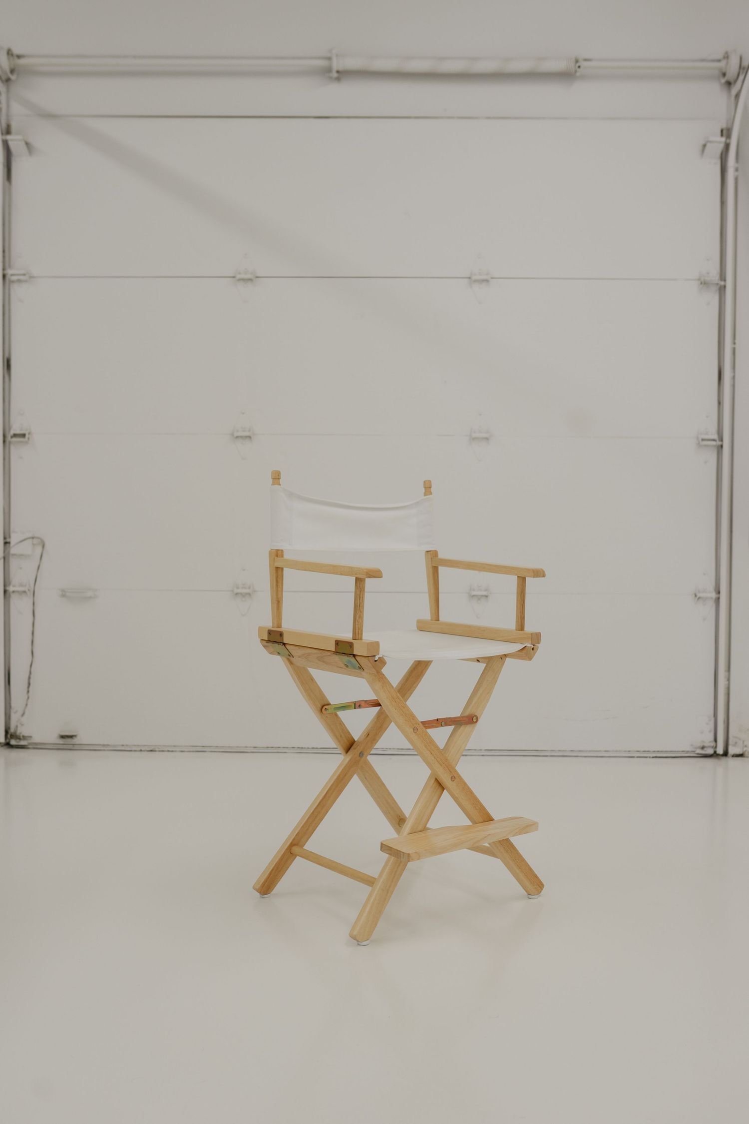 A wooden director's chair sits alone against a white backdrop in a minimalist studio setting.